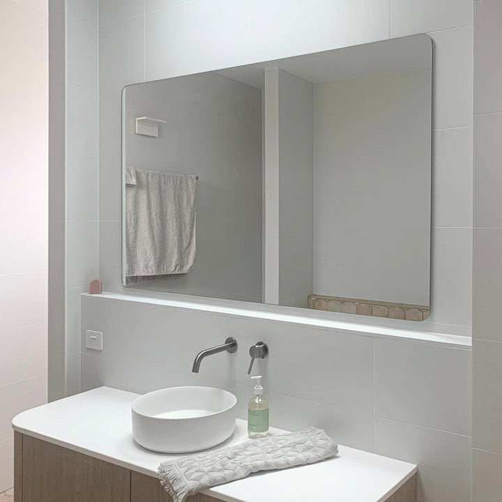 Frameless rectangular mirror with polished edge, wall-mounted mixer, and round basin on stone vanity in a bathroom.