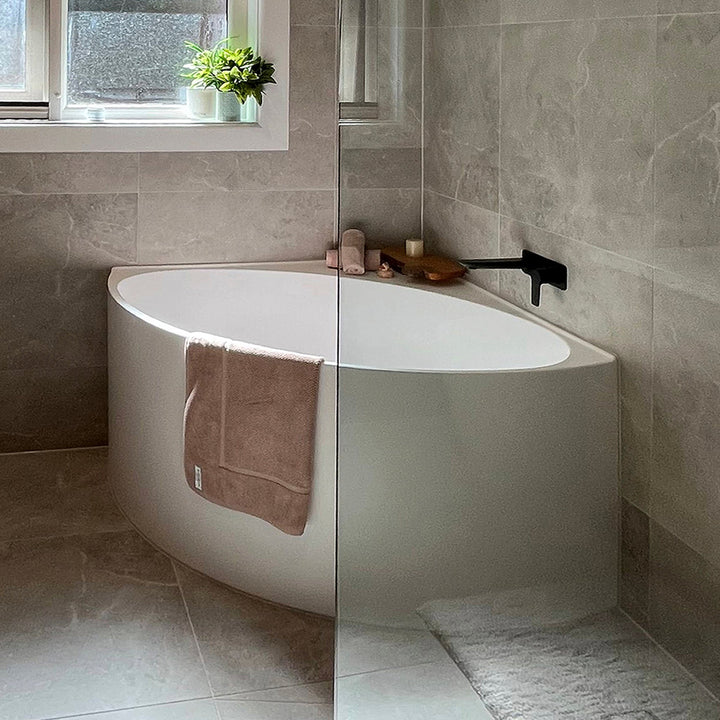 Angie Corner Fit Japanese Soaking Bathtub in a modern bathroom with grey stone tiles, walk-in shower and matte black wall bath spout.